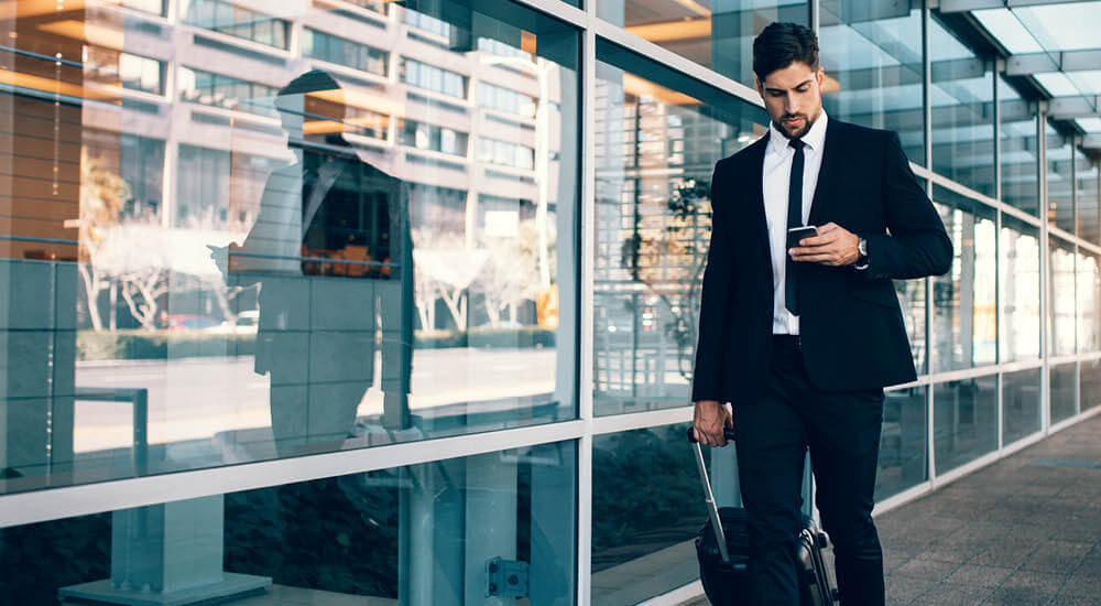 Business man pulling his carry-on luggage using his mobile phone